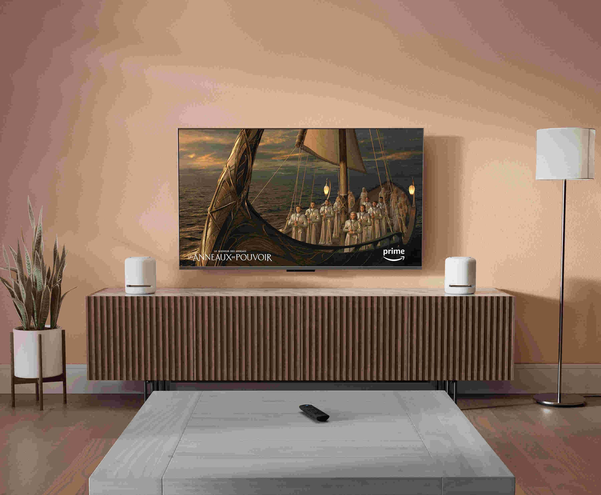 Une télévision HD fixée au mur dans un salon moderne affiche le contenu Prime Video, à côté de 2 enceintes Echo Studio cylindriques maillées de 17 cm de large et 20 cm de haut, plates sur le dessus et la base, et avec 4 boutons sur le haut.